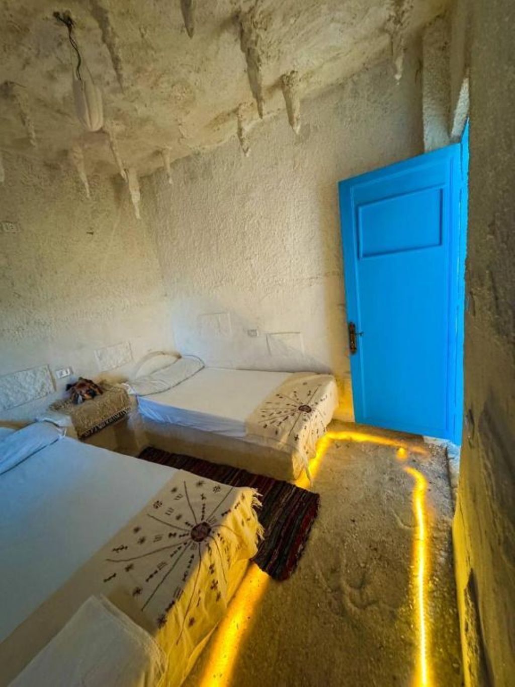 Ein rustikaler Raum mit zwei Betten, einer blauen Tür und einer strukturierten Decke.