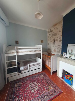 Une chambre d’enfant avec des lits superposés, un tapis, une cheminée et un mur en pierre.