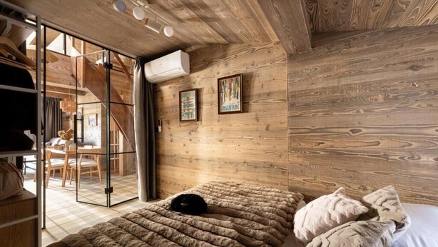 A wooden cabin interior with a bed, a dining area, and a sliding glass door leading to a balcony. - Zenya Krupówki 34c (Zakopane)