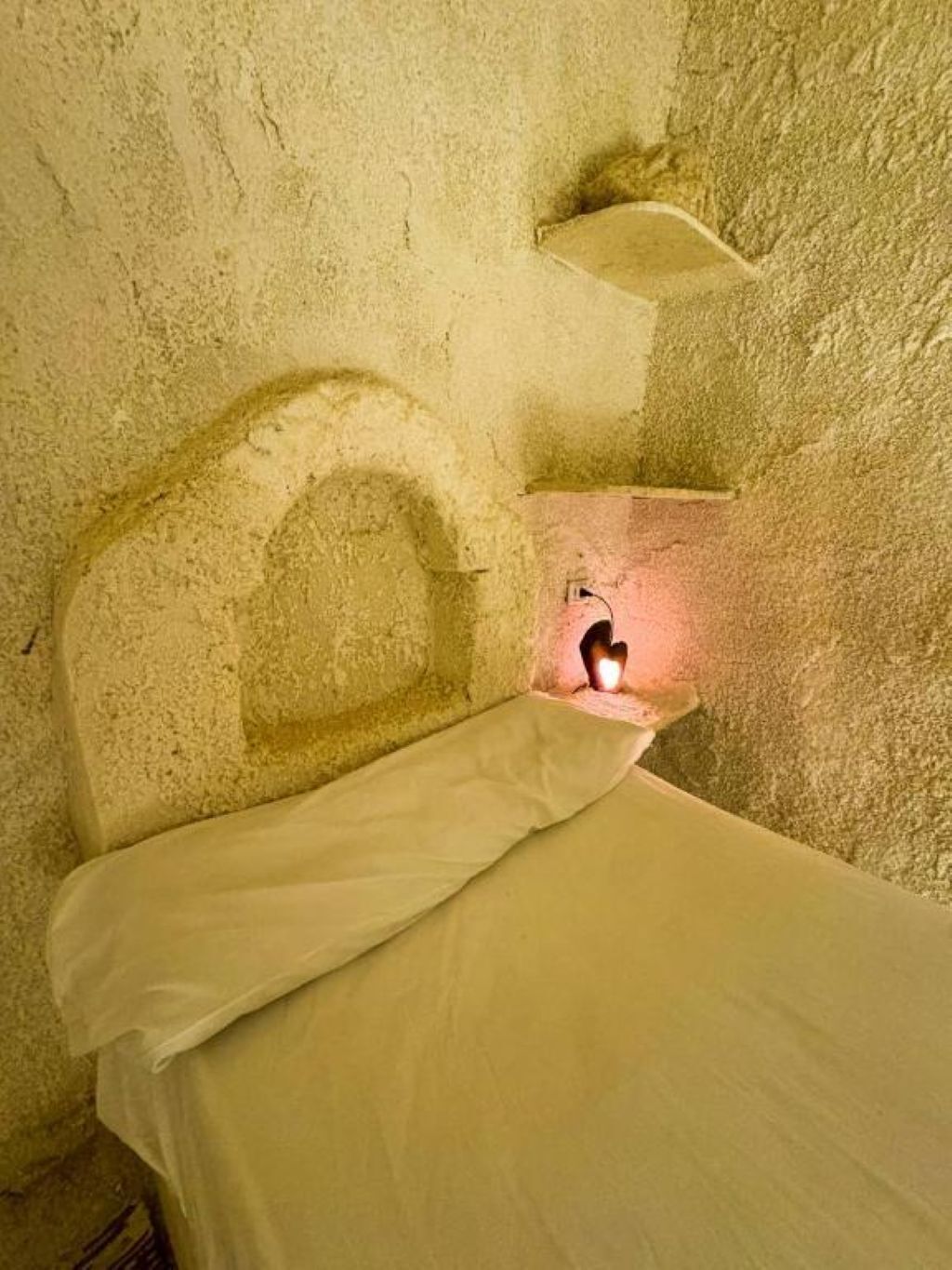 Un lit simple dans une chambre dont un mur est texturé et qui possède une petite fenêtre.