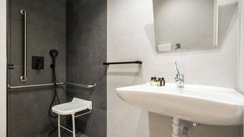 A modern bathroom with a shower, grab bars, a white sink, and a mirror.