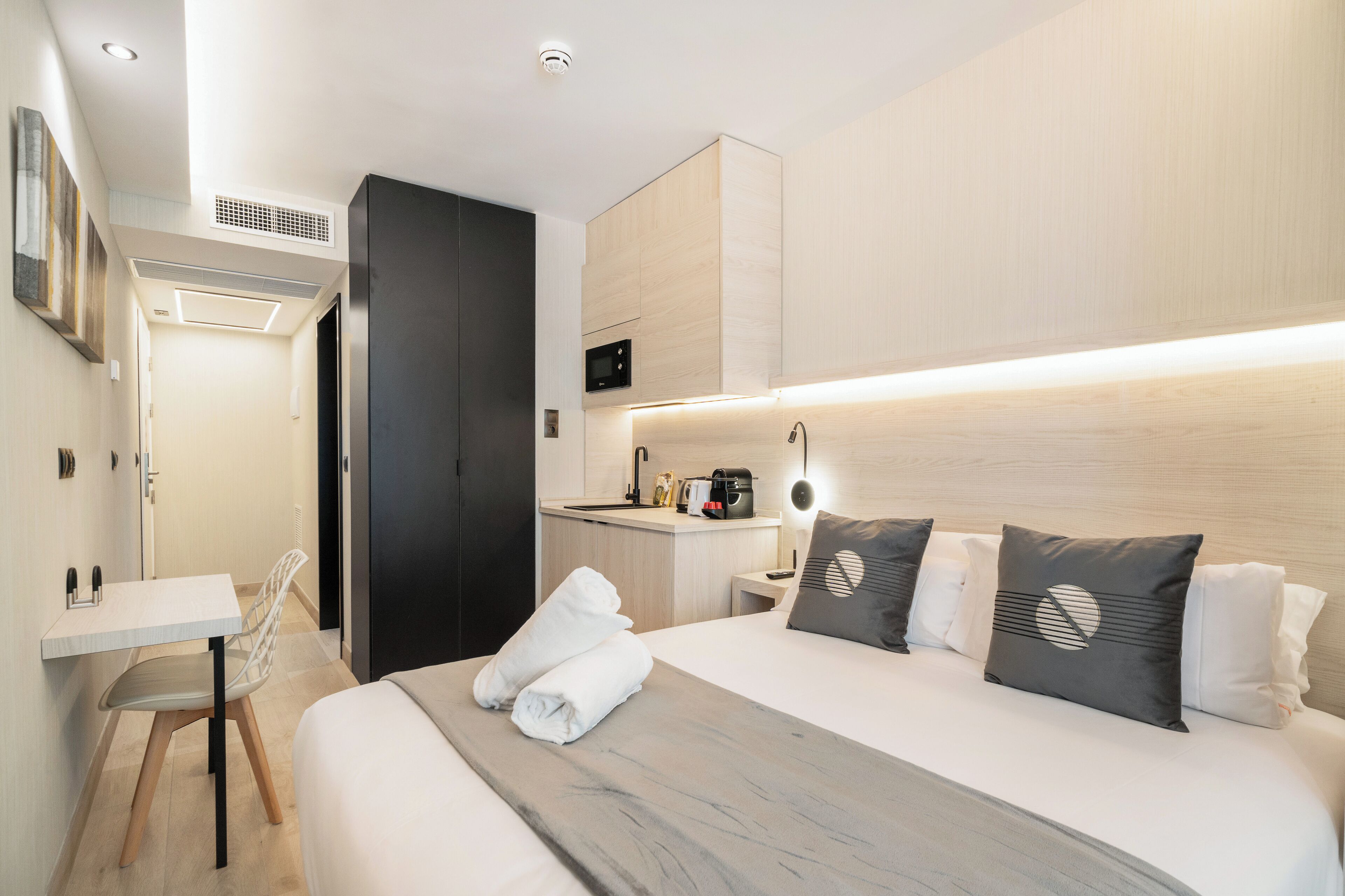 Ett modernt hotellrum med en säng, ett nattduksbord och ett litet pentry.