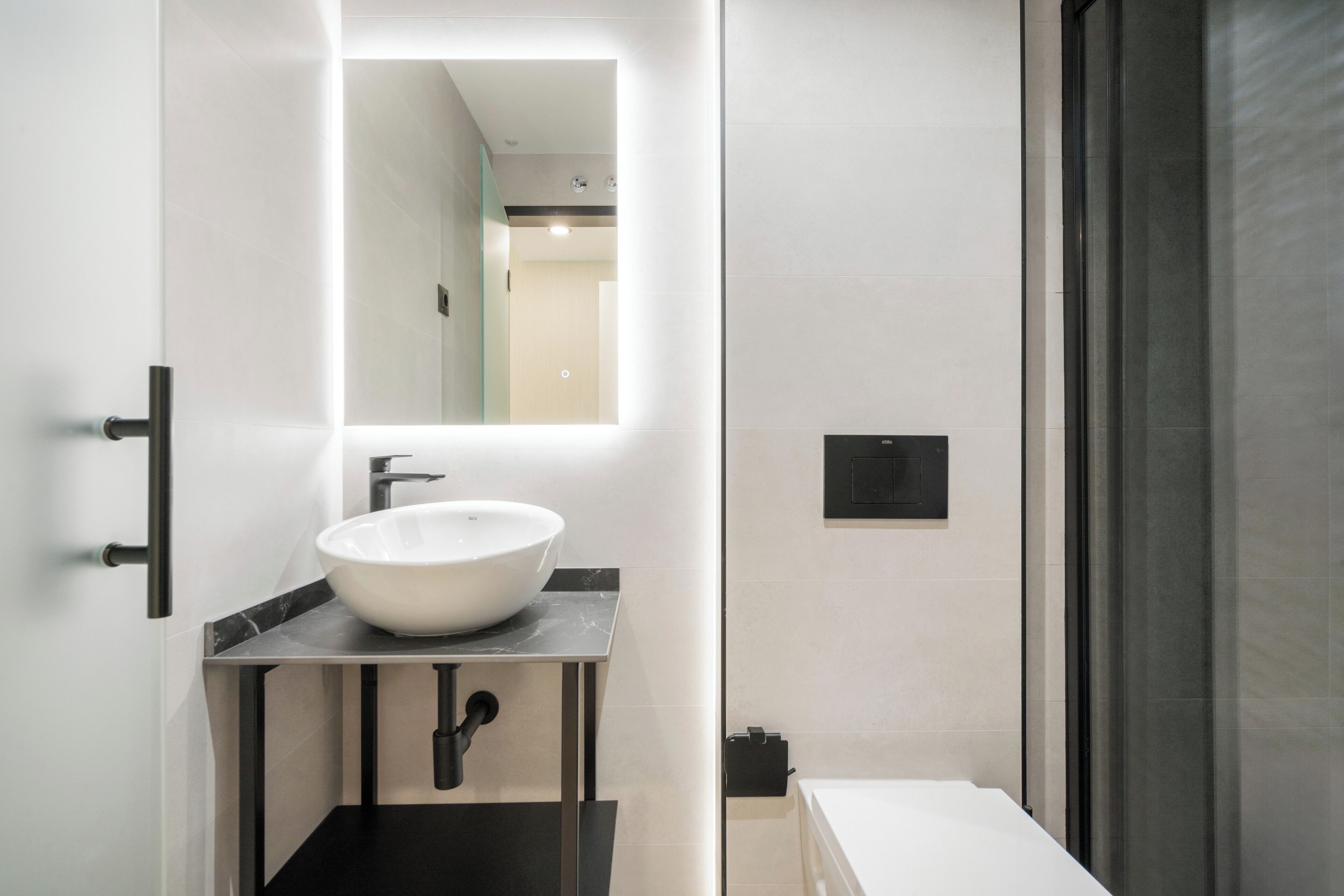 A modern bathroom with a large mirror, a white sink, and a shower area.