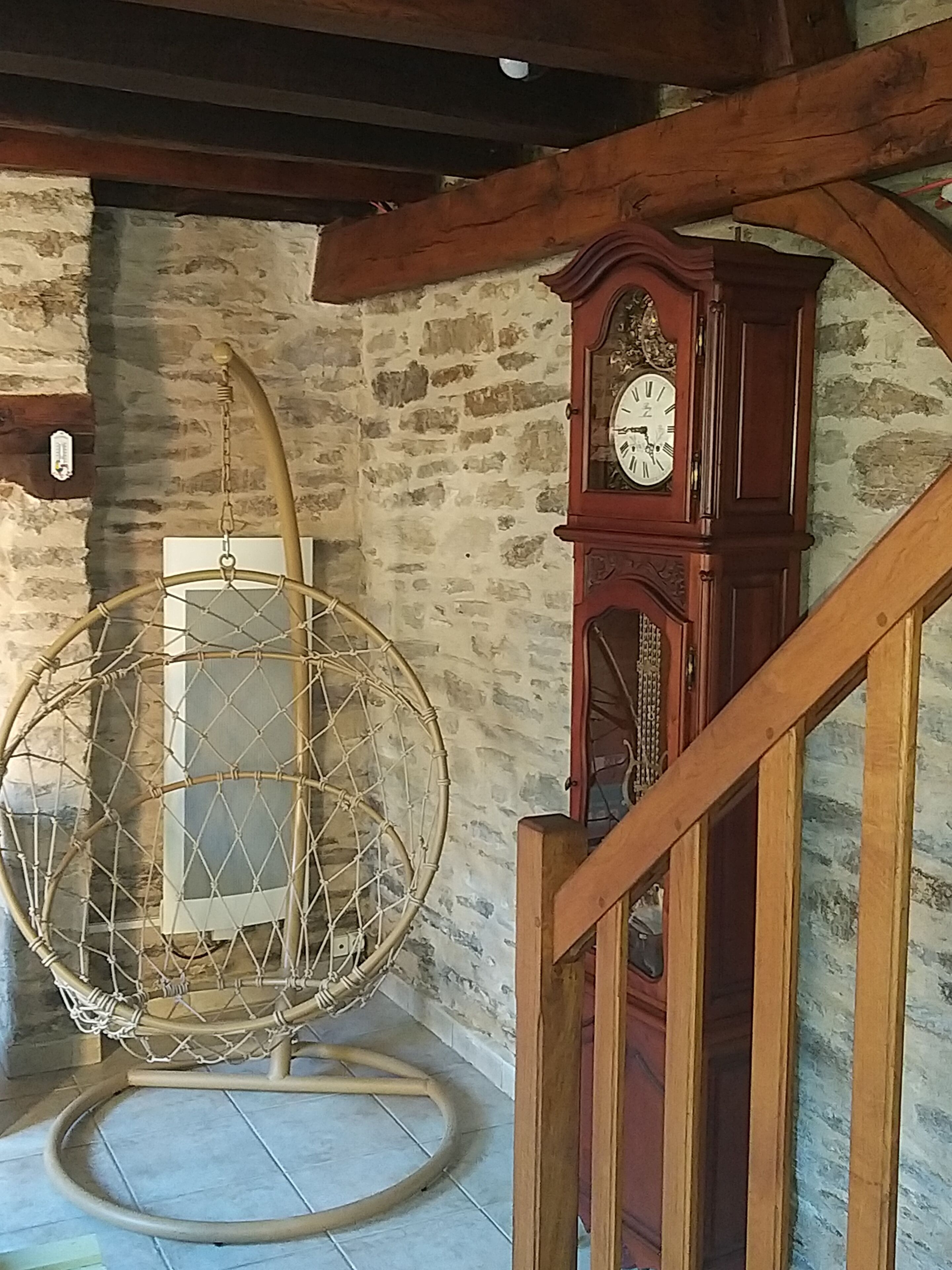 Une pièce avec un mur en pierre, un plafond en bois, un fauteuil suspendu et une horloge en bois.
