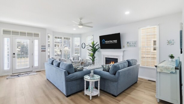 A living room with a sectional sofa, a fireplace, a television, and a ceiling fan. - Gold Coast 4BR Condo • Steps to Beach & Boardwalk (Ocean City)
