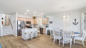A modern kitchen with a central island, white cabinetry, and a dining area with white chairs and a table. - Gold Coast 4BR Condo • Steps to Beach & Boardwalk (Ocean City)
