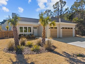 Una casa moderna de dos pisos con garaje, rodeada de un jardín ajardinado con palmeras y plantas de agave.