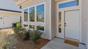 A modern two-story house with large windows, a front door, and a small garden area. - Private Pool, Carolina Beach Rental, Dog Friendly, Luxury Finishes, Sleeps 9 (Carolina Beach)