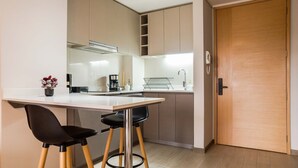 Une cuisine moderne avec un plan de travail blanc, deux tabourets de bar noirs et une porte en bois.