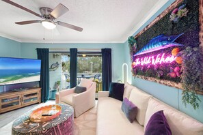 A living room with a large flat-screen TV, a ceiling fan, a sofa, and a wall-mounted aquarium. - The Wild Wahoo by Liquid Life (Orange Beach)
