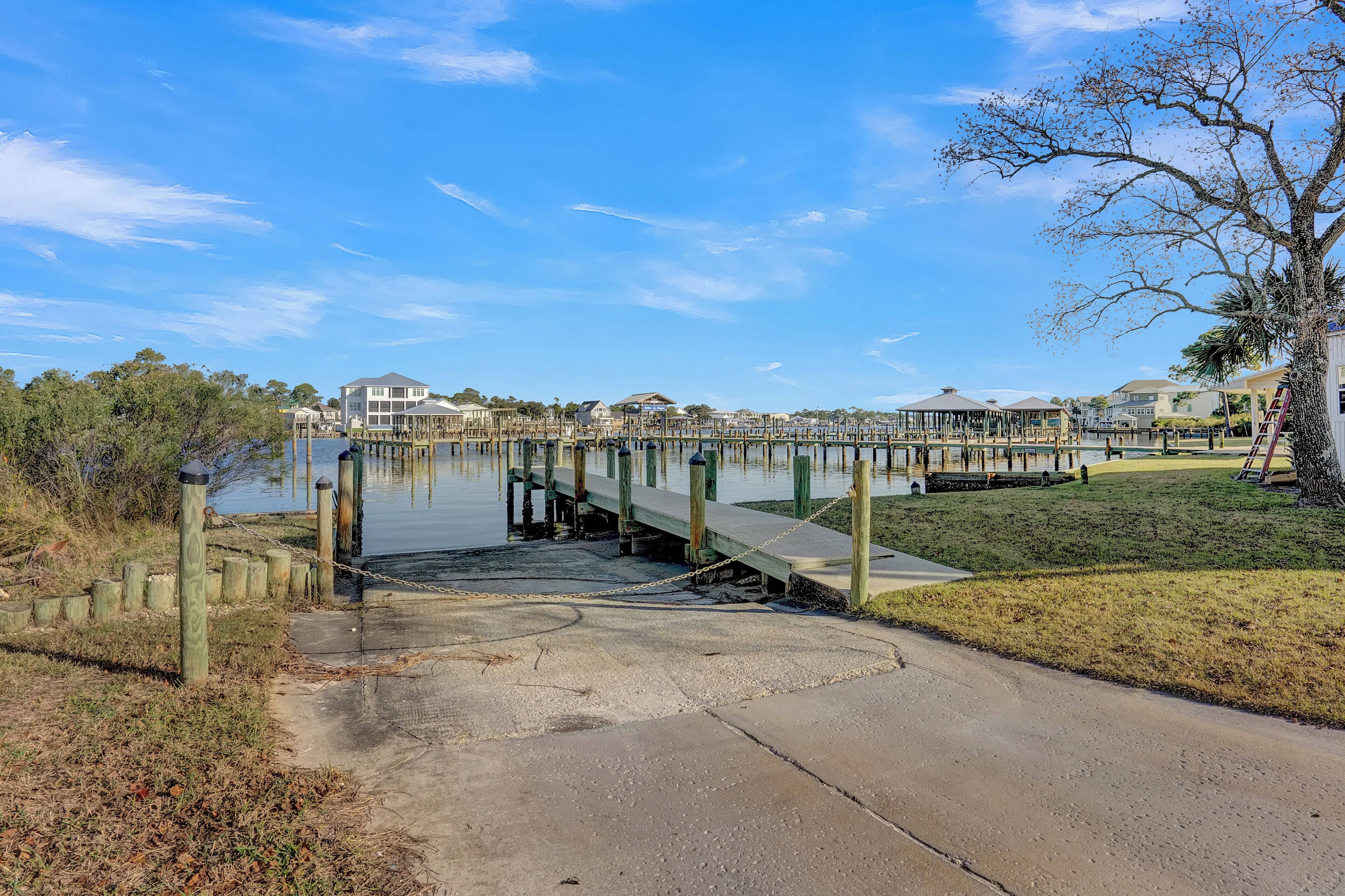 A waterfront park with a wooden pier, a concrete walkway, and a grassy area.