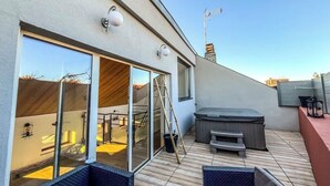 Een modern terras buiten met een whirlpool, zitgedeelte en een glazen deur naar de binnenruimte.