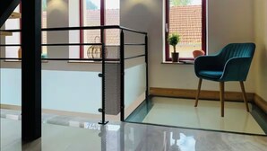 Een moderne kamer met een glazen vloer, een blauwe stoel en een trap met een metalen leuning.