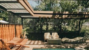 Un espace piscine doté d’une terrasse en bois, de deux chaises longues et d’un coin salon abrité.