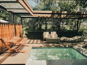 Een zwembadgedeelte met een houten terras, twee loungestoelen en een overdekte zithoek.