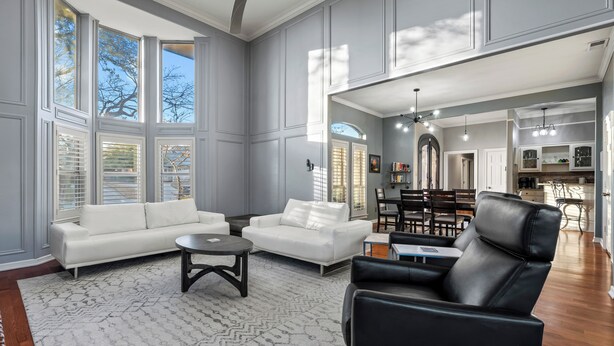 A spacious living room with a large window, a ceiling fan, and a dining area in the background. - Laurel Lane Oasis / Pool + Game Area + Near DFW (Bedford)