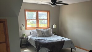 Une chambre à coucher avec un lit, une fenêtre, un ventilateur de plafond et une table de chevet avec une lampe.