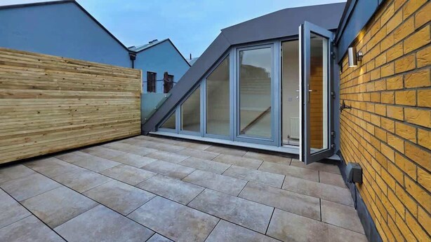 Une terrasse sur le toit, agrémentée d’une clôture en bois, d’une porte coulissante en verre et d’un mur en briques.
