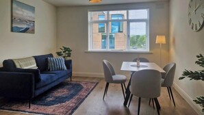 A living room with a sofa, a dining table with chairs, a window with blinds, and a clock on the wall. - Trendy 1-Bed near Luas & City Centre (Dublin 6)