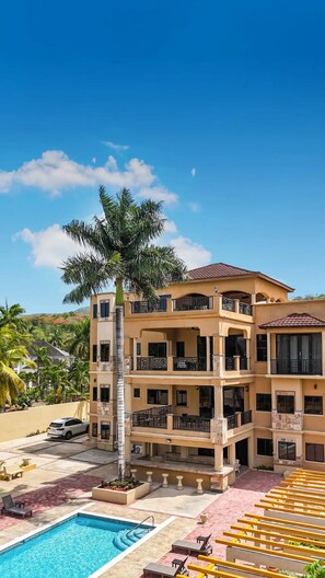 A multi-story hotel with a pool, outdoor seating, and a palm tree.