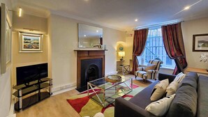 A living room with a fireplace, a television, a sofa, and a window with curtains.