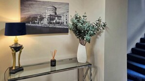 A glass console table with a decorative lamp, a vase with green foliage, and a bottle of reed diffuser.