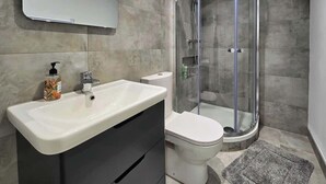 Et badeværelse med en hvid vask, toilet og brusekabine med glasvægge.