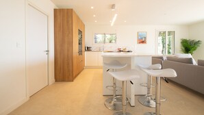 Une cuisine moderne avec des plans de travail blancs, des armoires en bois et un coin bar doté de tabourets blancs.