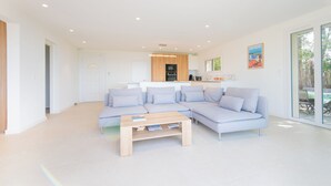 A modern living room with a light-colored sectional sofa, a wooden coffee table, and a kitchen in the background. - Villa du Meinier - Sea view 8 guests (Sainte-Maxime)