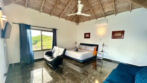 Una habitación con cama, sofá, sillón, ventilador de techo y ventana con cortinas.