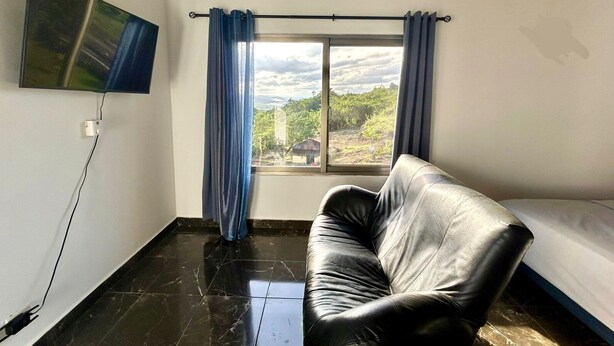 A room with a black leather sofa, a TV mounted on the wall, and a window with curtains. - 3-bedroom villa in beautiful Rio San Juan with cool breeze (Rio San Juan)