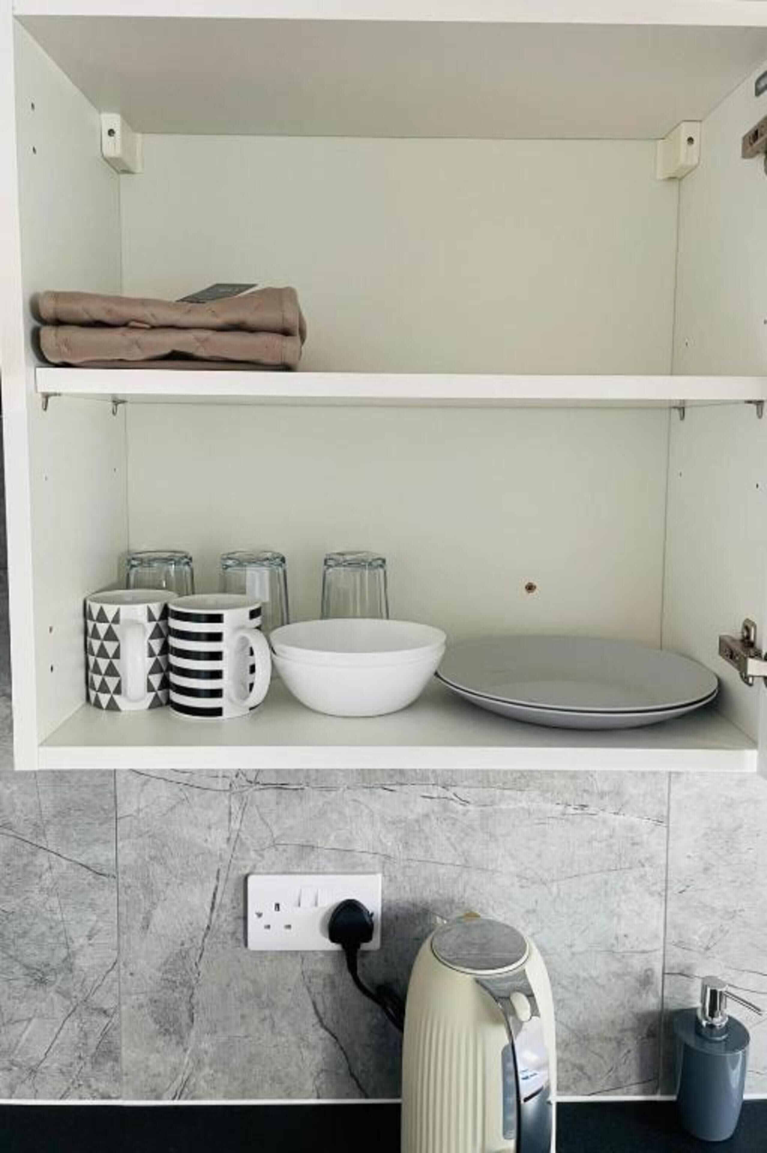 A kitchen with a white countertop, a kettle, a coffee maker, and a sink.