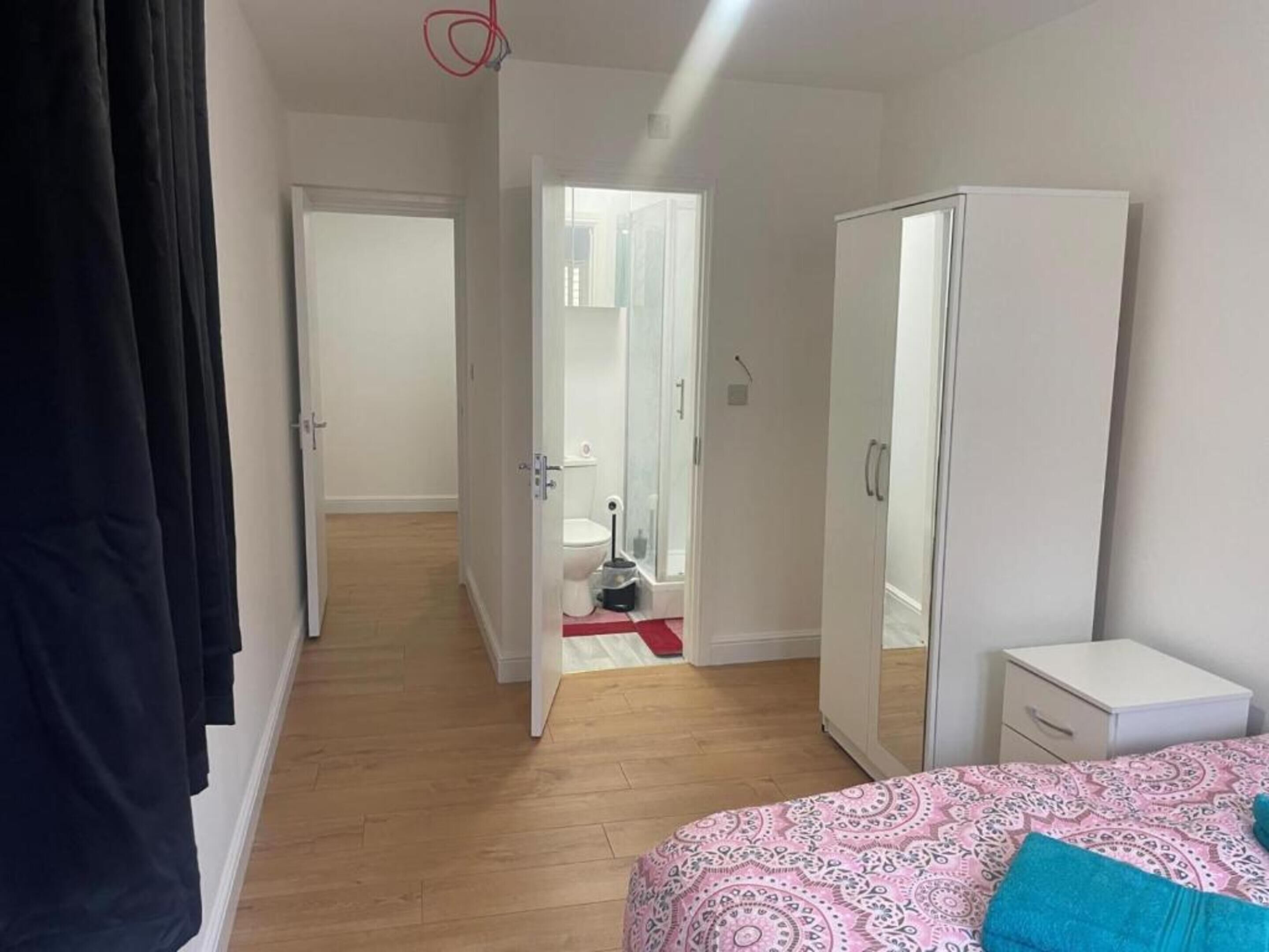 Un dormitorio con cama, armario, mesita de noche y baño visible a través de una puerta abierta.