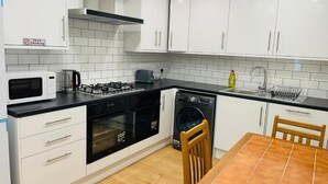A modern kitchen with white cabinets, a microwave, stove, oven, and dishwasher. - OYO Dorset House At Upton Park (London)