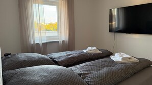 Ein Hotelzimmer mit zwei Betten, einem an der Wand befestigten Fernseher und einem Fenster mit Vorhängen.