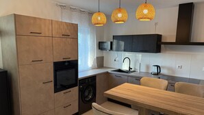 Eine moderne Küche mit Holzschränken, einem Einbauofen, einer Waschmaschine, einem Spülbecken und einem Esstisch mit Stühlen.