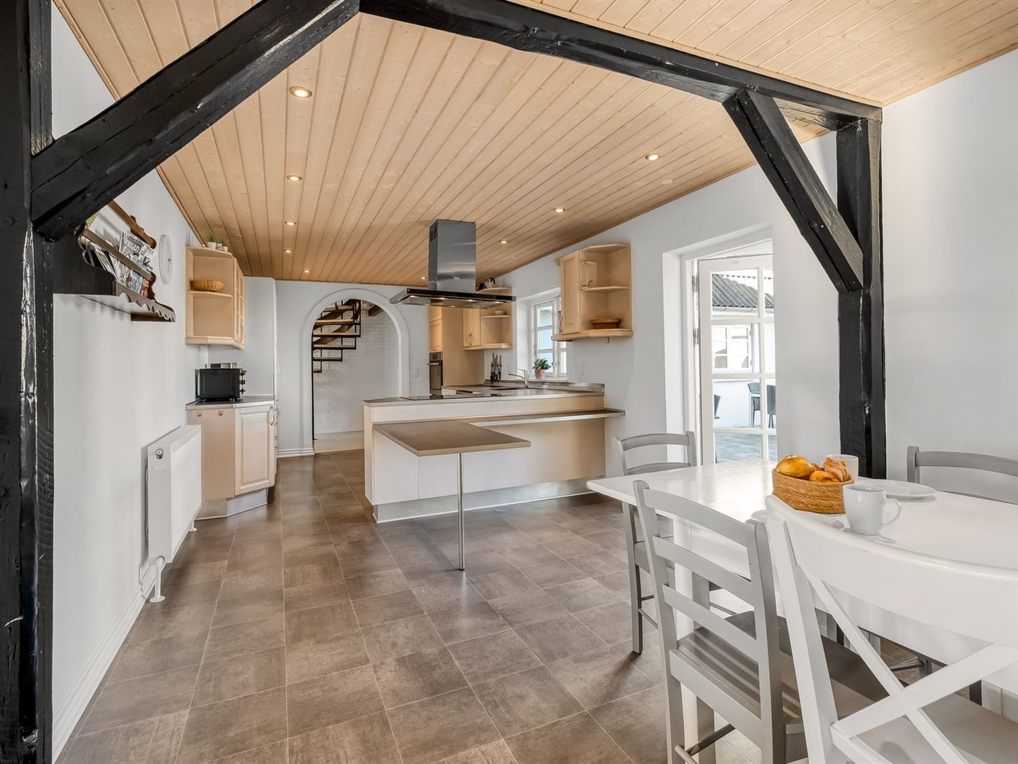 A modern kitchen with a central island, wooden beams, and a dining area with a table and chairs.