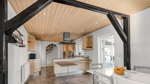 Een moderne keuken met een centraal eiland, houten balken en een eethoek met tafel en stoelen.