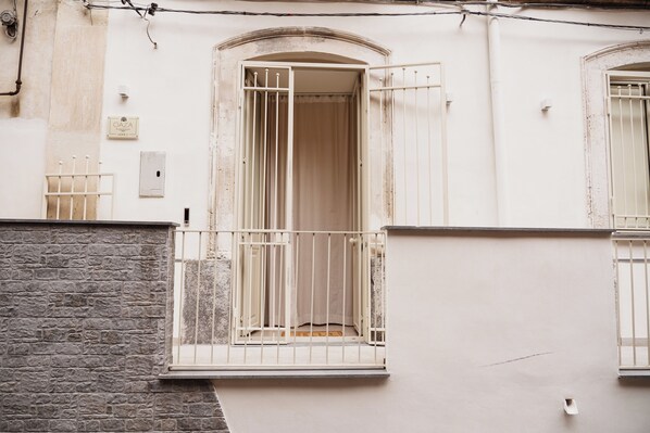 Un edificio con fachada de piedra, un balcón con barandilla de metal y una puerta con cortina.