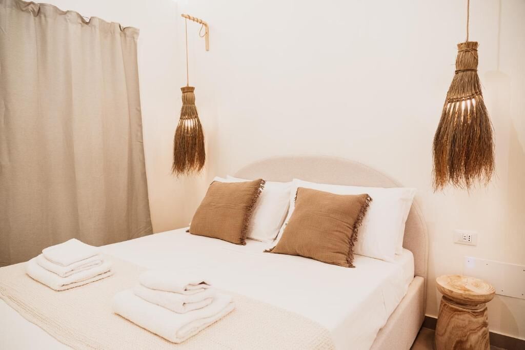 Una cama bien hecha con ropa de cama blanca y marrón, dos lámparas colgantes con borlas y una mesita de noche redonda de madera.