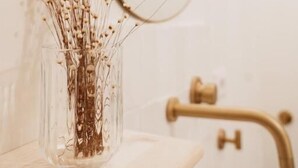 A bathroom with a clear glass vase containing dried flowers on the counter, a gold faucet, and a round mirror. - oaza Catania (Catania)