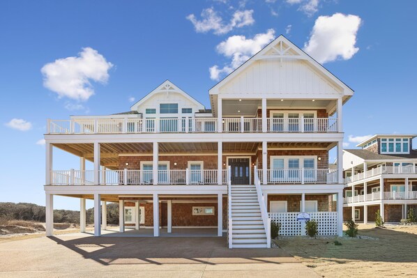 A multi-story beachfront property with balconies, a covered front porch, and a staircase leading to the upper levels. - Dennis -- Brand New in 2026! (Corolla)