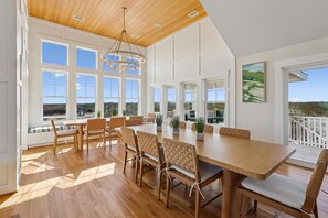 A spacious dining area with a long wooden table, multiple chairs, and large windows offering a view of the landscape. - Dennis -- Brand New in 2026! (Corolla)