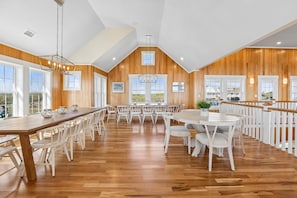 Uma sala de jantar espaçosa com paredes de madeira, cadeiras brancas e uma mesa comprida.
