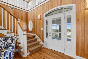 Un interior de fusta amb una escala, una porta blanca amb panells de vidre i una cadira amb un disseny decoratiu.