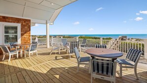 A covered outdoor deck with a wooden table and chairs, a view of the ocean, and a white railing. - Fearing -- Brand New Oceanfront -- Ready for 2026! (Corolla)