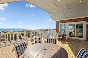 Um deck de madeira com móveis de exterior, uma mesa e vista para o oceano.