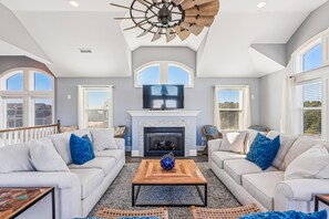 Ein geräumiges Wohnzimmer mit Kamin, zwei Sofas mit blauen Kissen, einem Couchtisch und einem Deckenventilator.