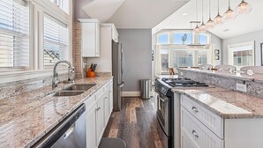 Une cuisine moderne dotée de plans de travail en granit, d’appareils électroménagers en acier inoxydable et de luminaires suspendus.
