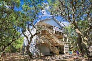 Ein zweigeschossiges Haus mit einer Holztreppe, die zu einem Balkon führt, umgeben von Bäumen.